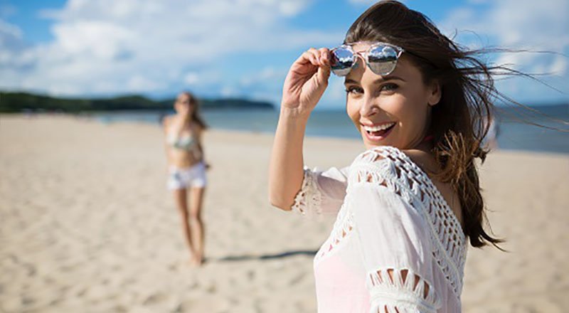 Happy beautiful woman standing on beach with friend laughing